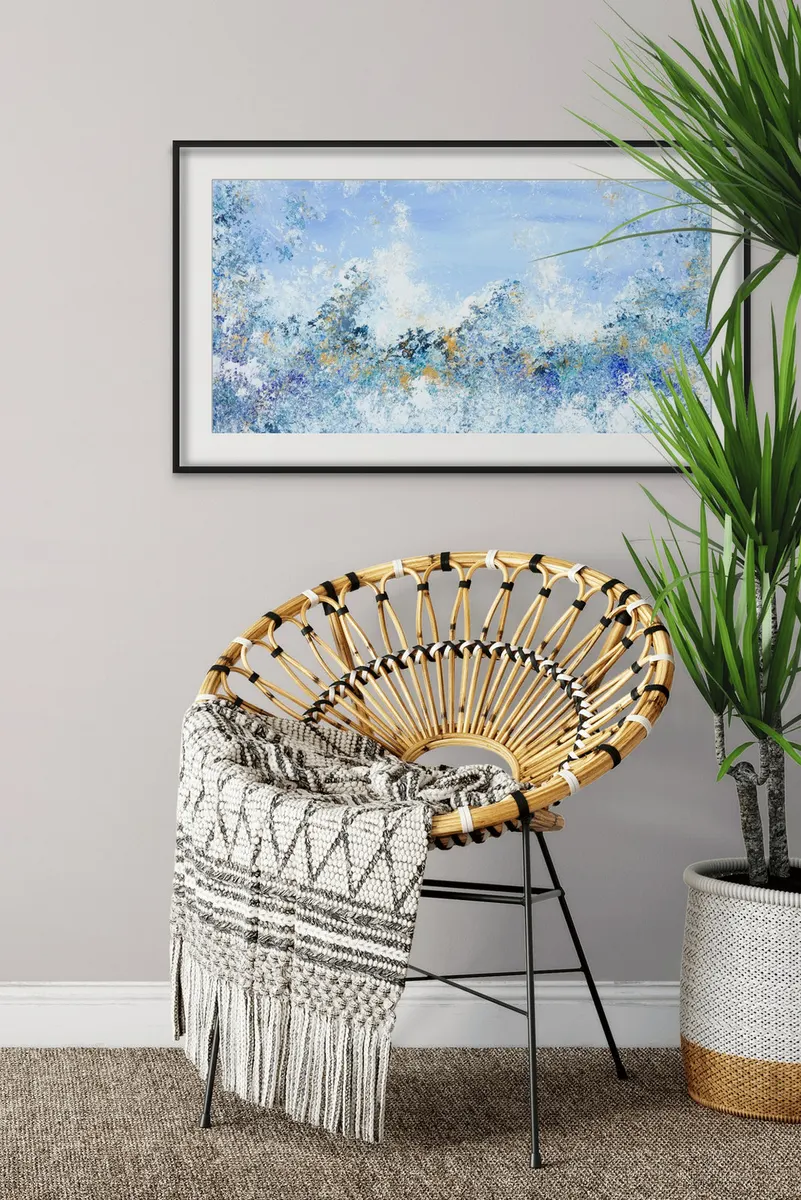 Framed blue and white abstract painting hanging above a rattan chair