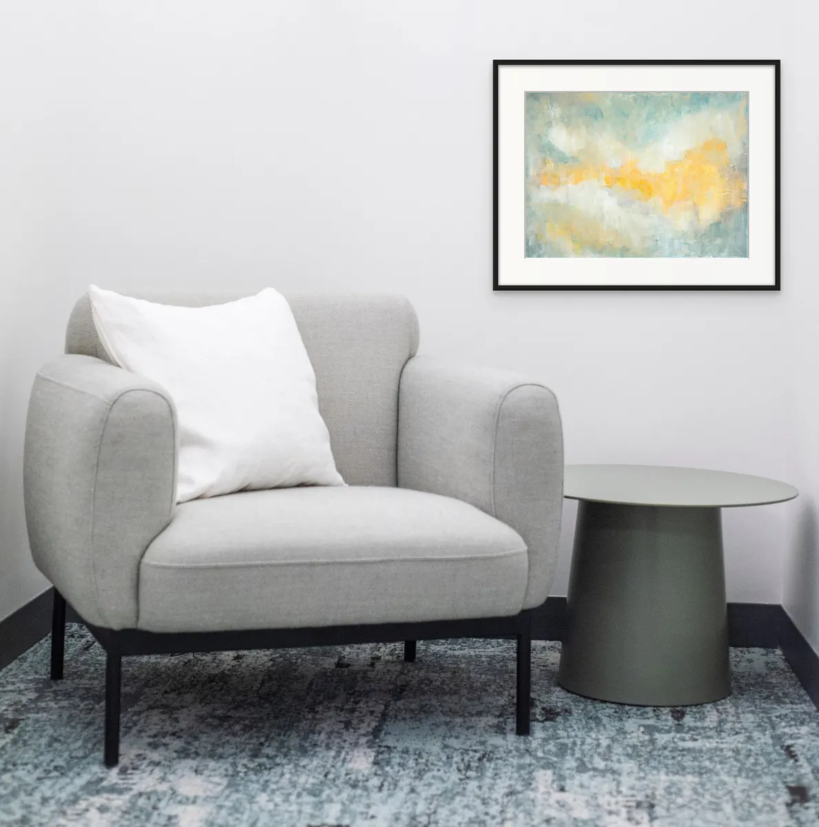 Framed abstract in soft blue and gold above a grey armchair