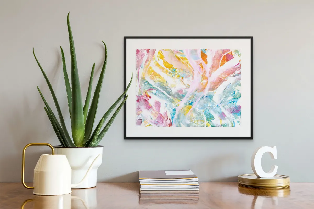 Framed pastel abstract in pink, yellow and blue on a desk wall