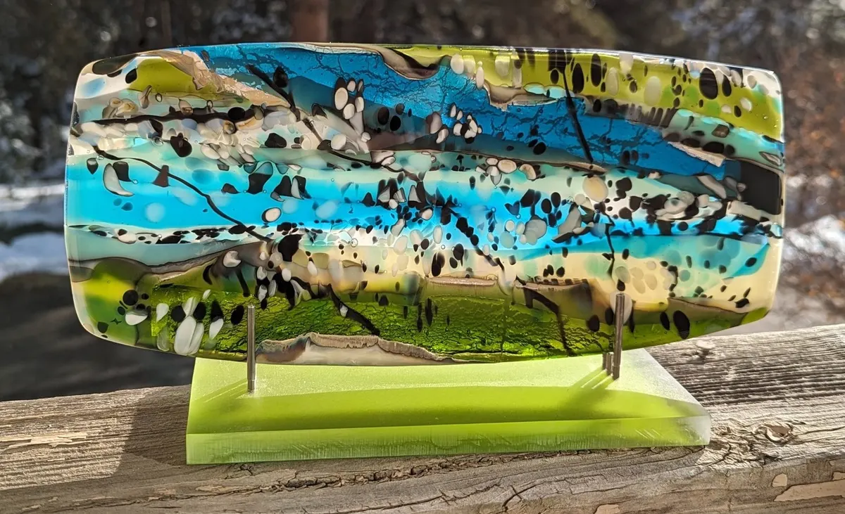 Fused glass panel in turquoise, olive and cream with speckled bands, on a green stand