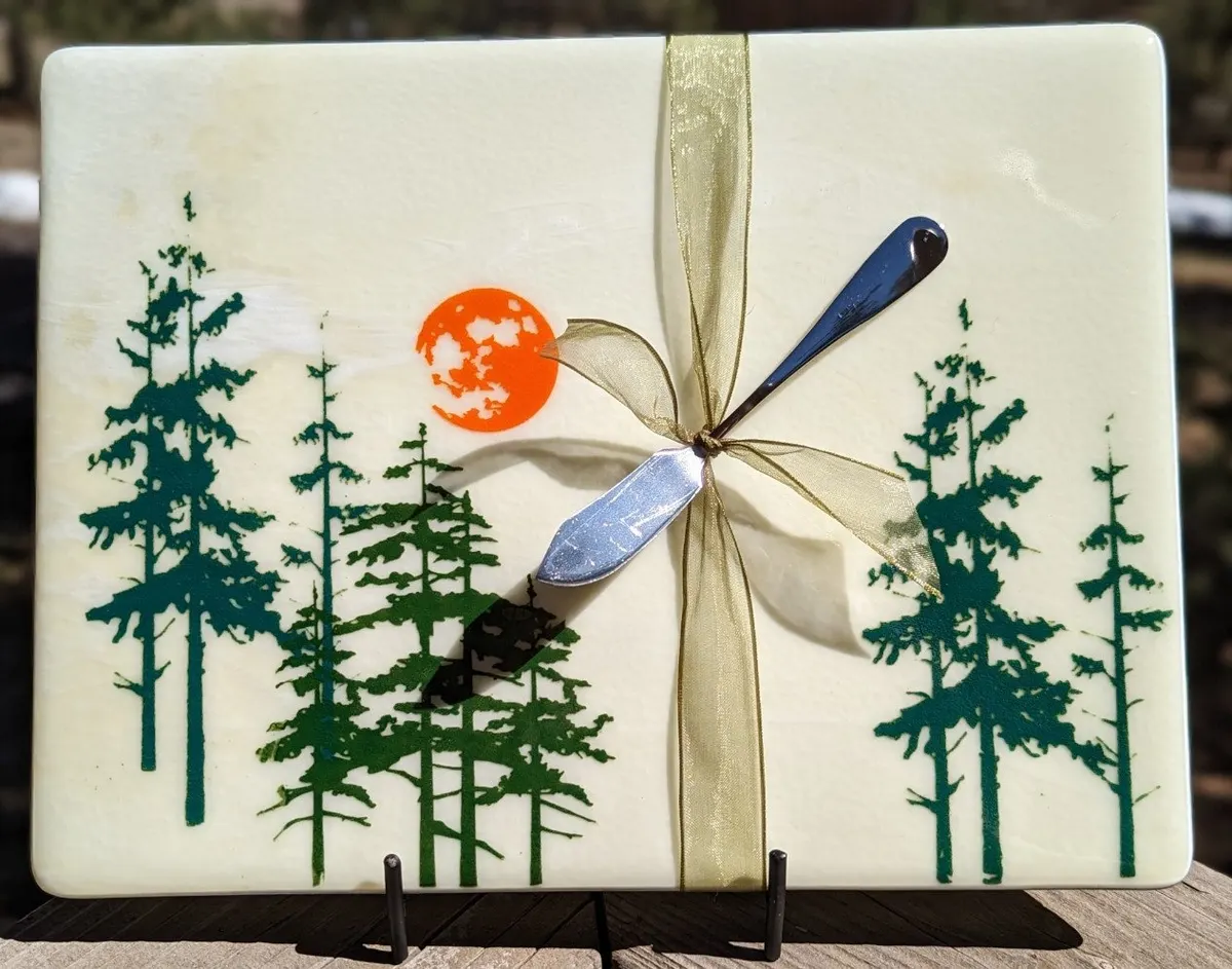 Cream fused glass panel with dark evergreens, an orange sun and a dragonfly