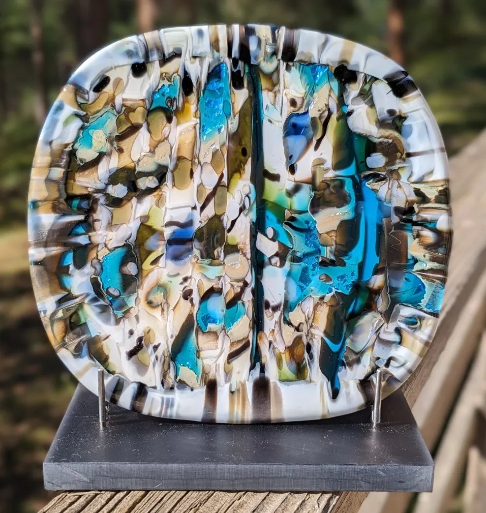 Round fused glass panel in mottled turquoise, cream and black on a stand