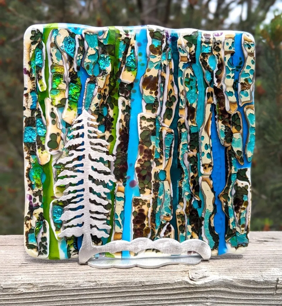 Tall fused glass panel in teal and green with a silver evergreen silhouette