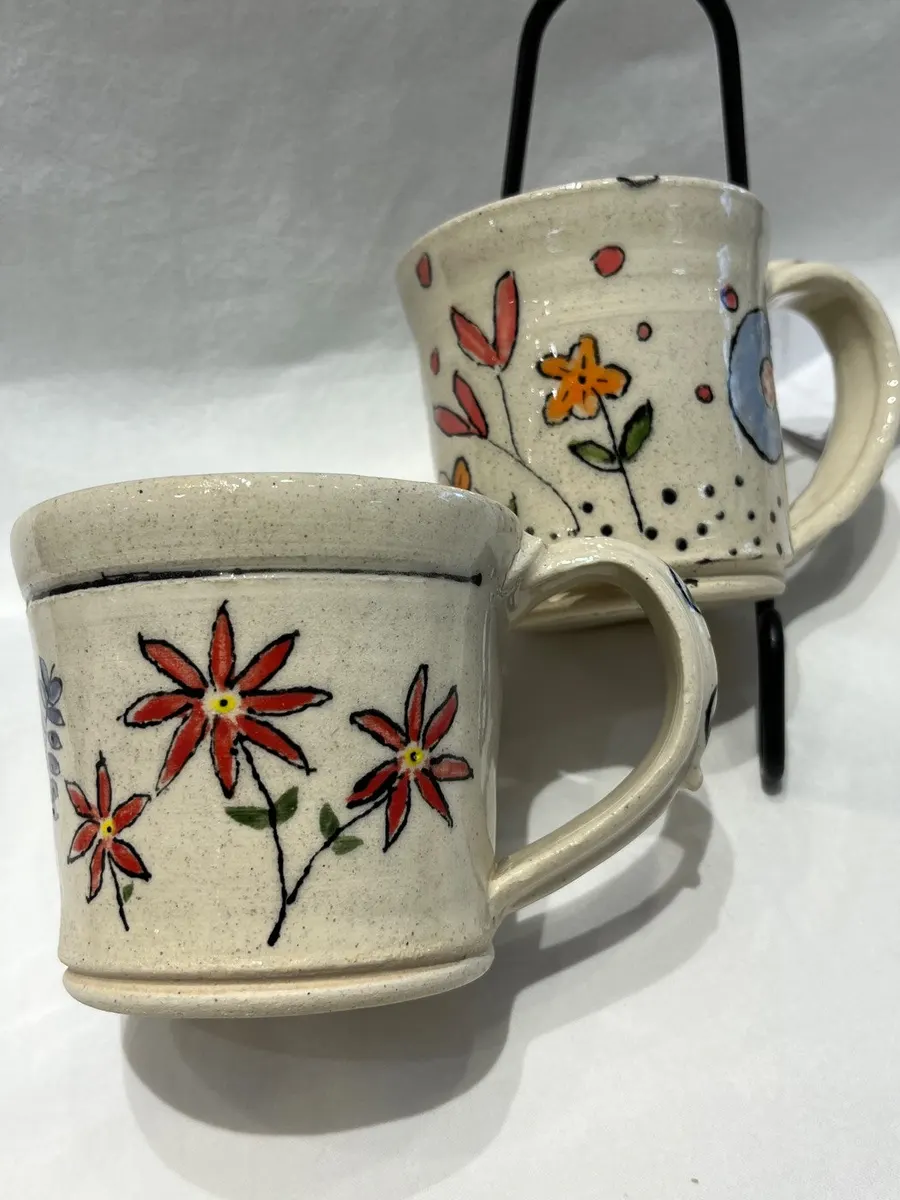 Two speckled mugs painted with red and orange daisies