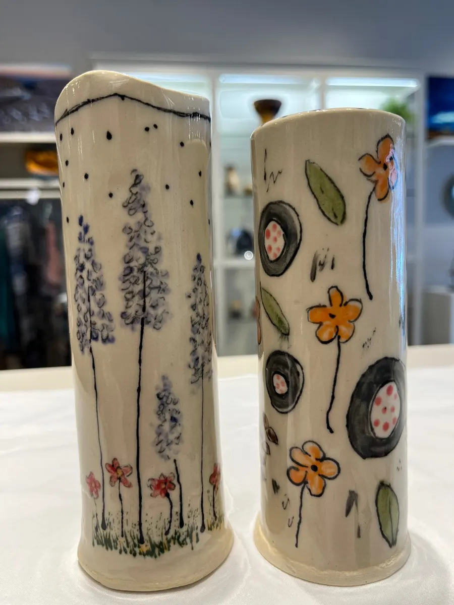 Two tall cylinder vases, one painted with lupines, one with dark round flowers