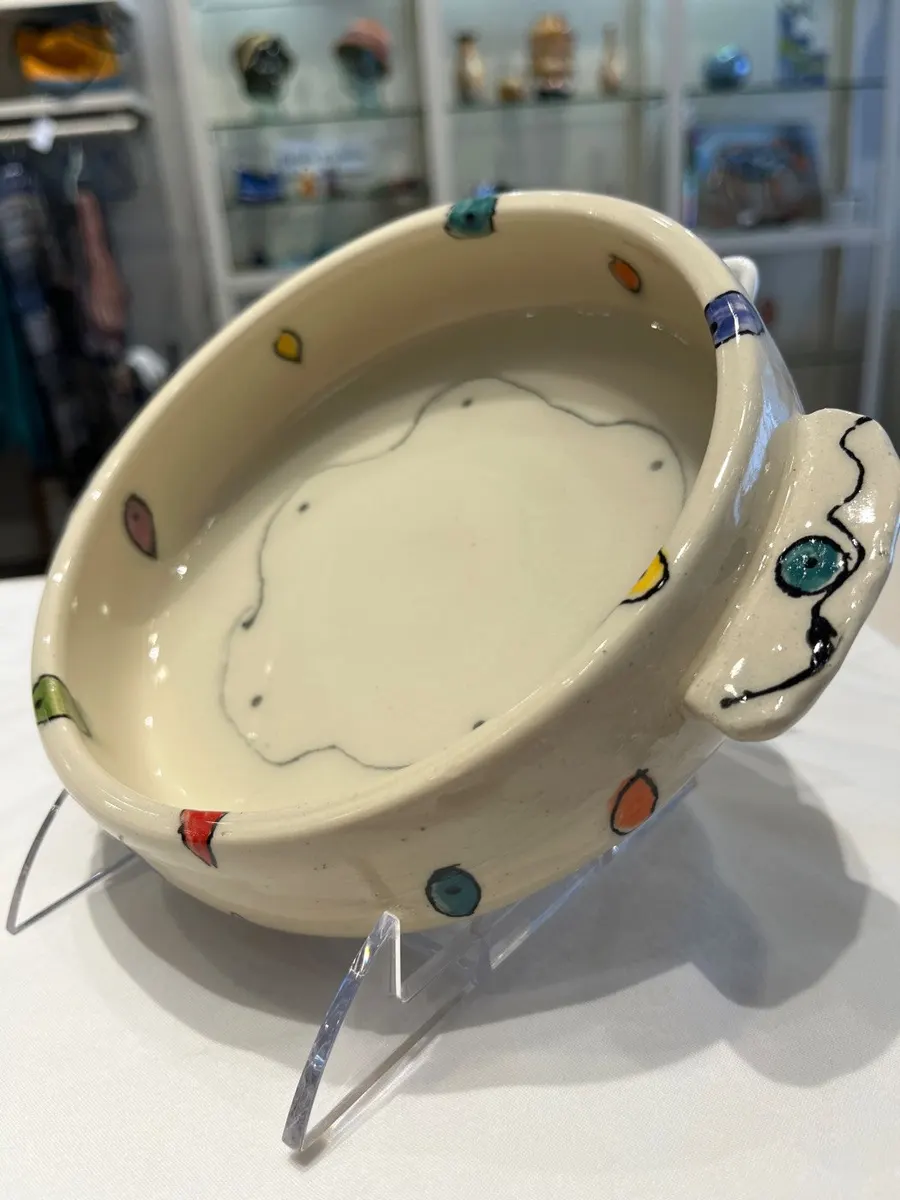 Shallow cream bowl with coloured dots around the rim and a curling handle