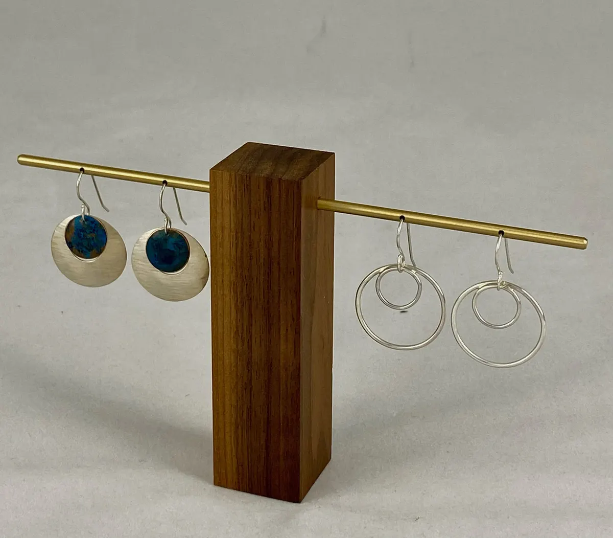Two pairs of earrings, teal enamel discs and plain silver hoops, on a wooden stand