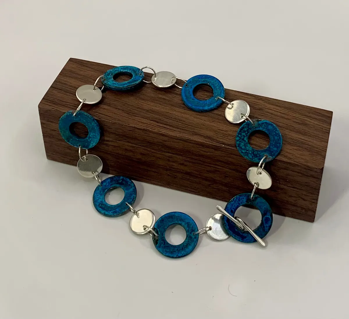 Bracelet of teal enamelled washers linked with silver discs on a wooden block