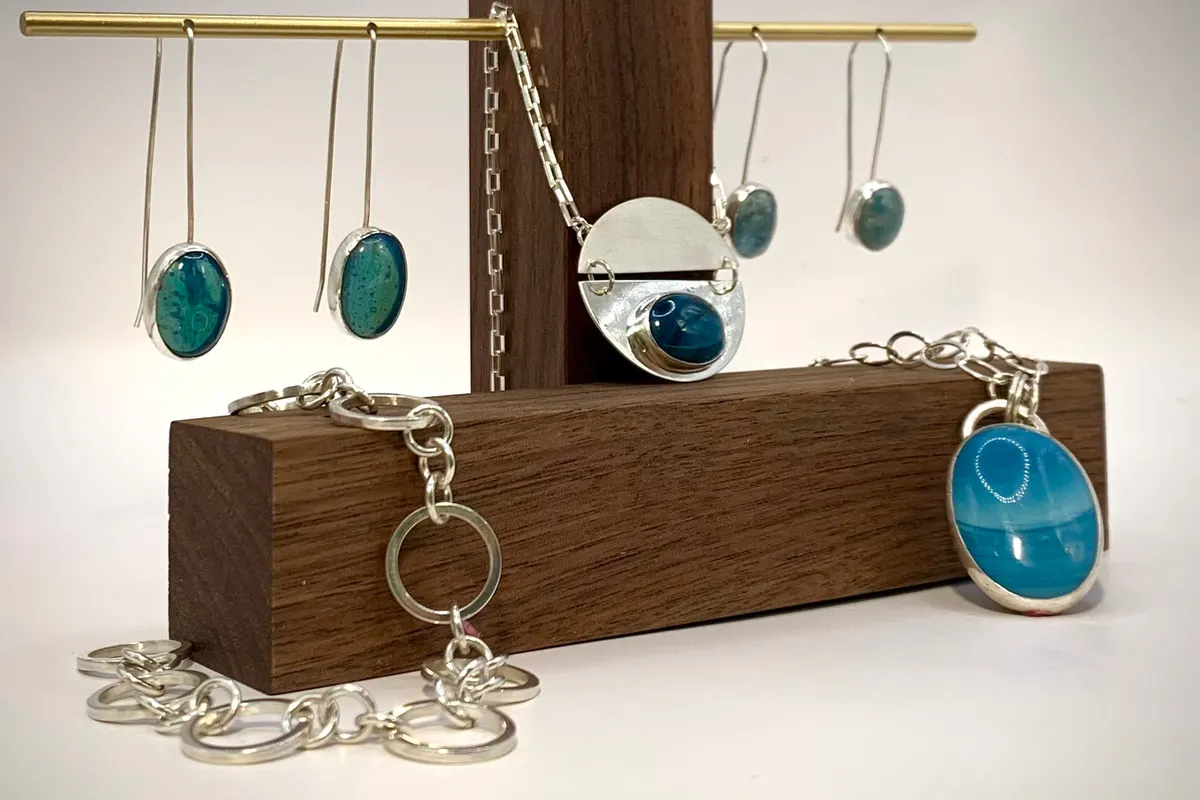 Teal enamel and silver earrings, bracelet and pendant on a wooden stand