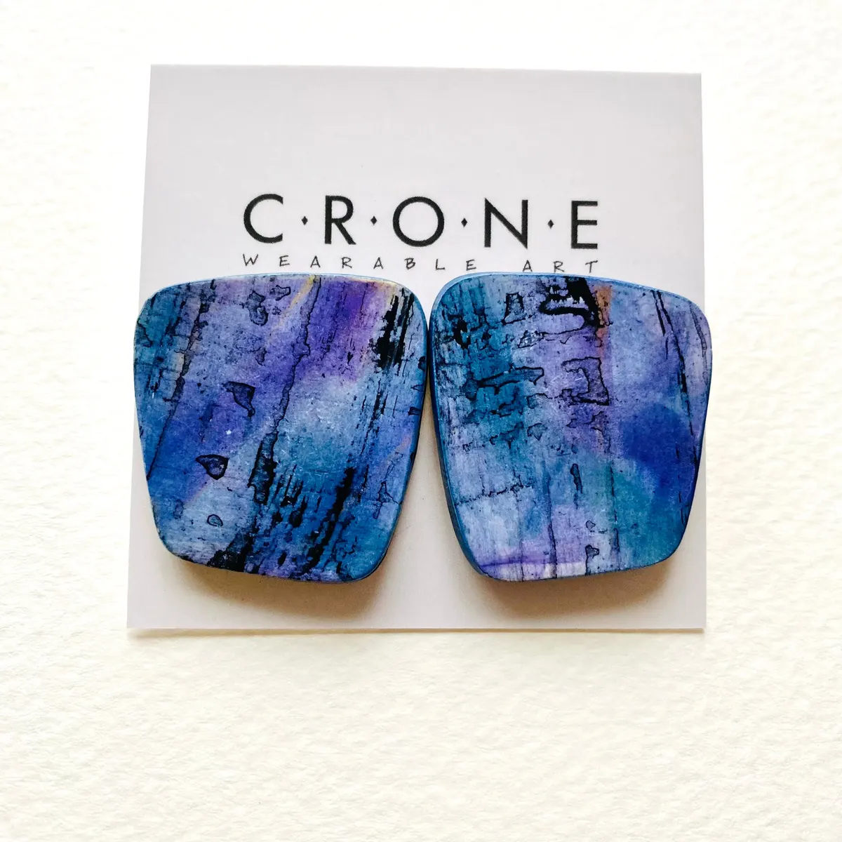 Pair of polymer clay earrings in mottled blue and purple on a Crone Wearable Art card