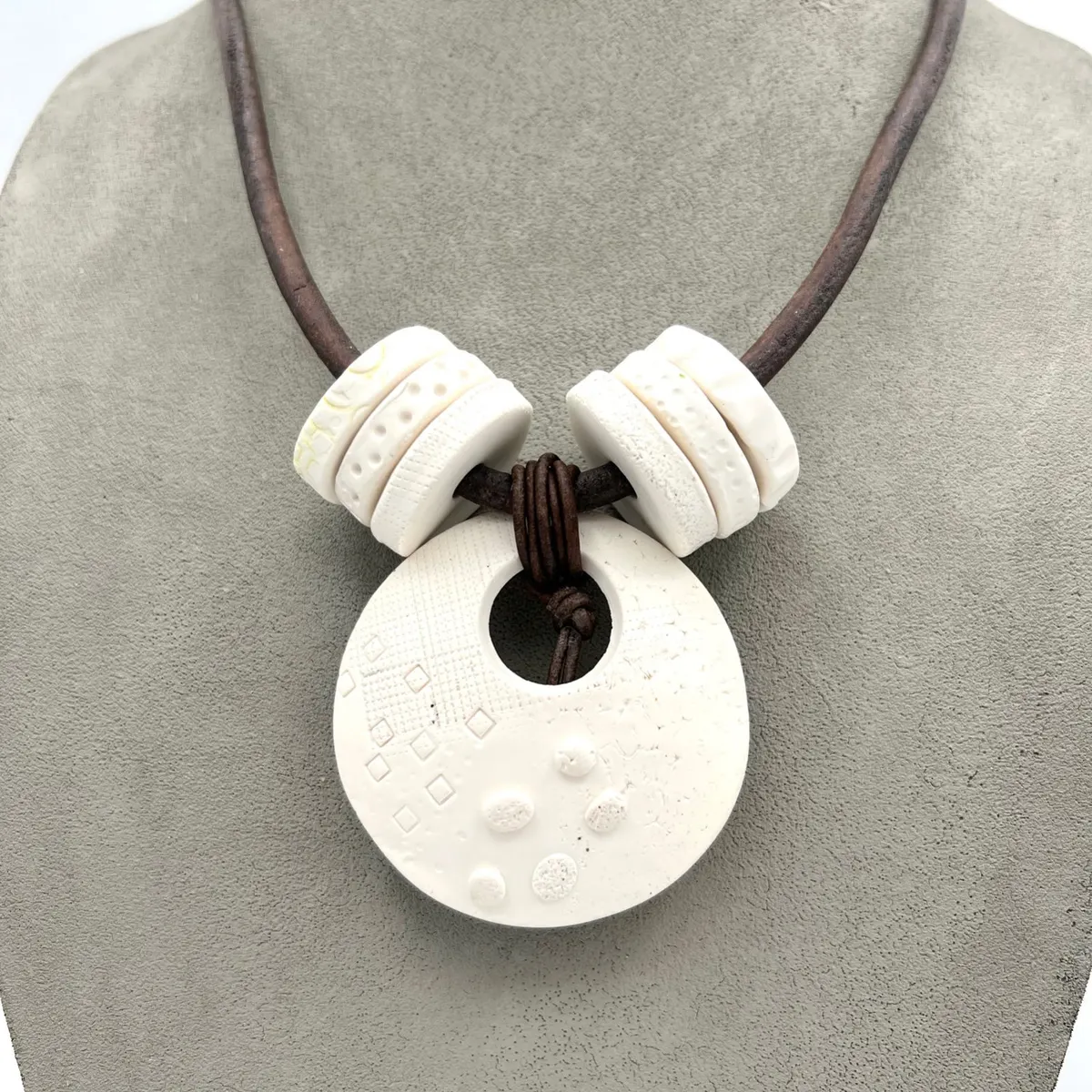 Round white polymer clay pendant with raised dots on a leather cord