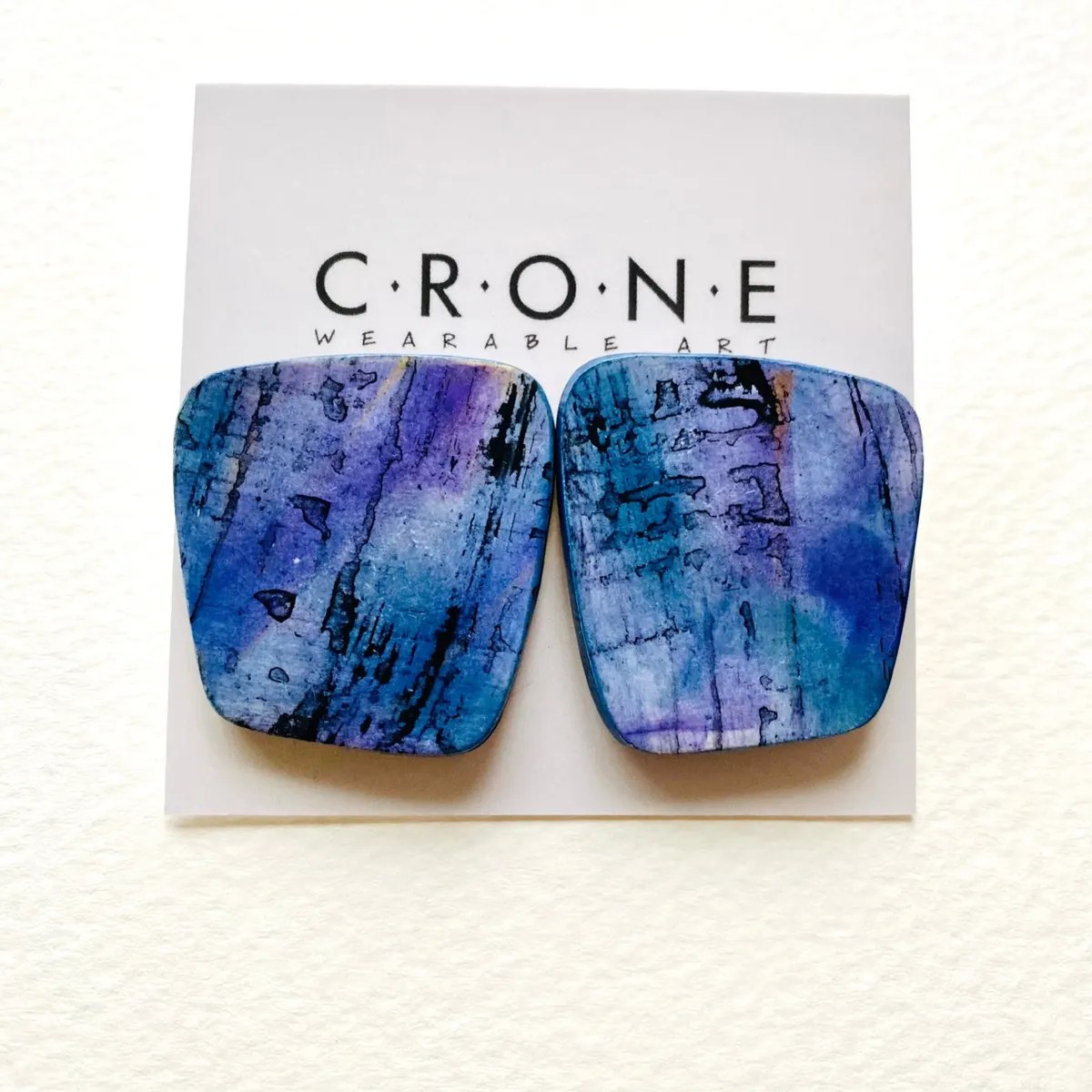 Pair of blue and purple mottled polymer clay earrings on a branded card