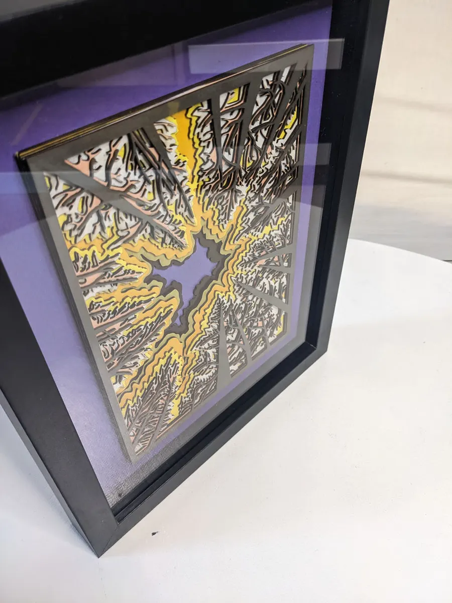 Layered laser-cut forest scene on a purple ground, angled in its frame