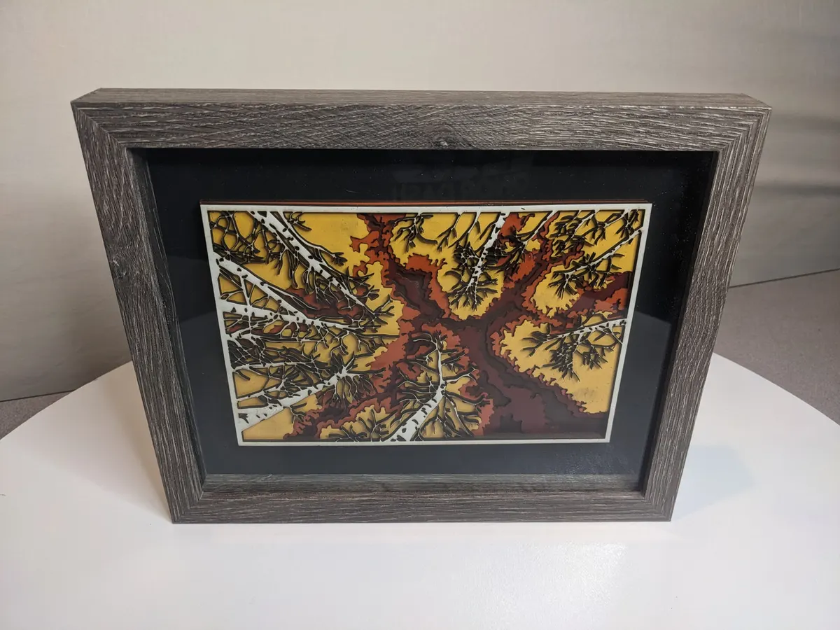 Layered laser-cut tree canopy in amber and rust, weathered wood frame