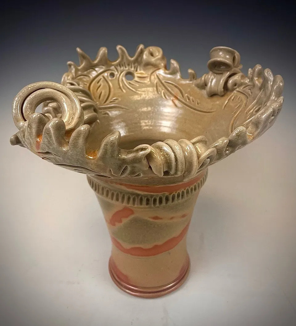 Tall footed vessel with sculpted scrollwork around the rim
