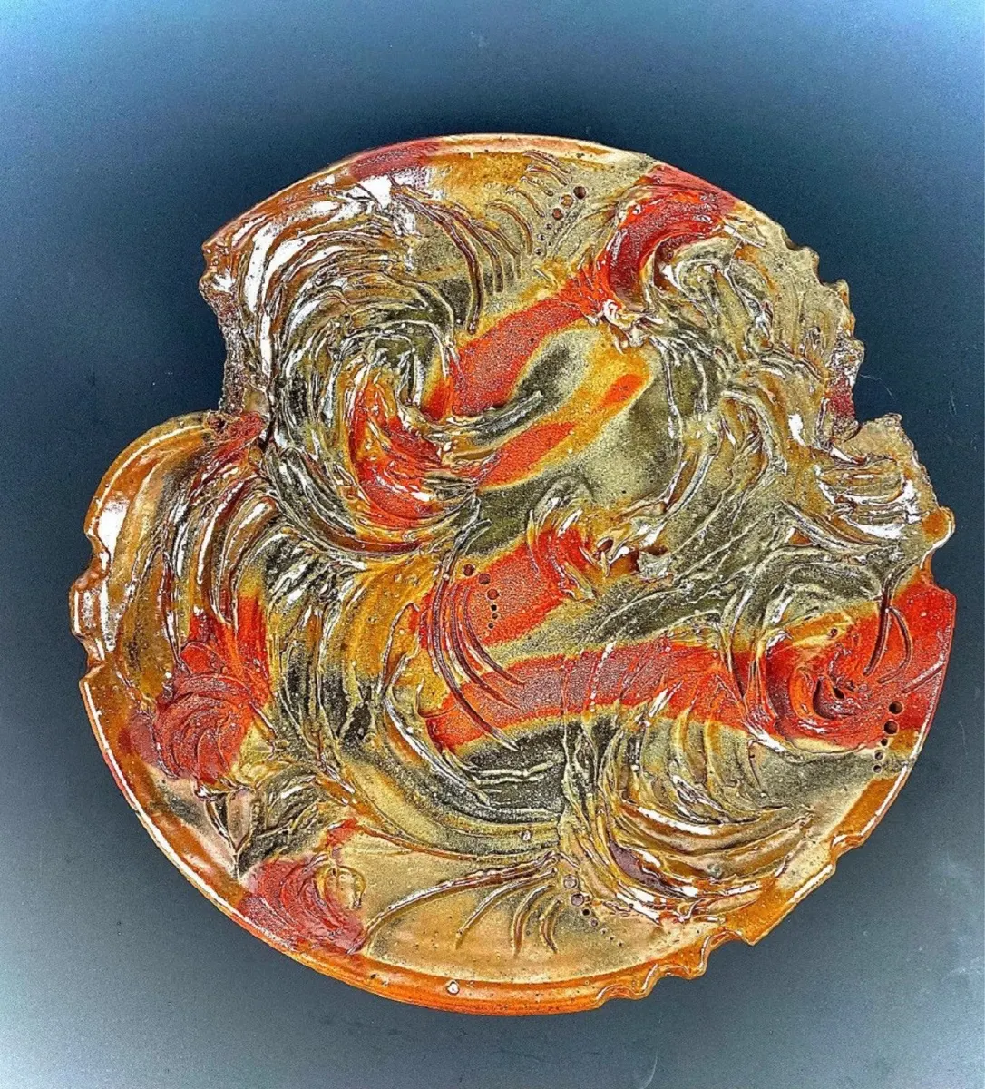 Round wall platter with swirling carved relief in red and gold