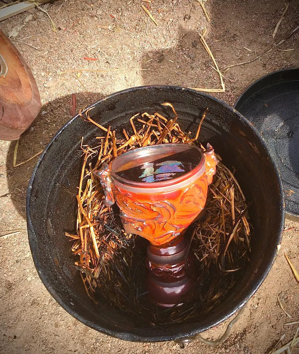Vessel resting in a bed of straw inside a metal firing barrel