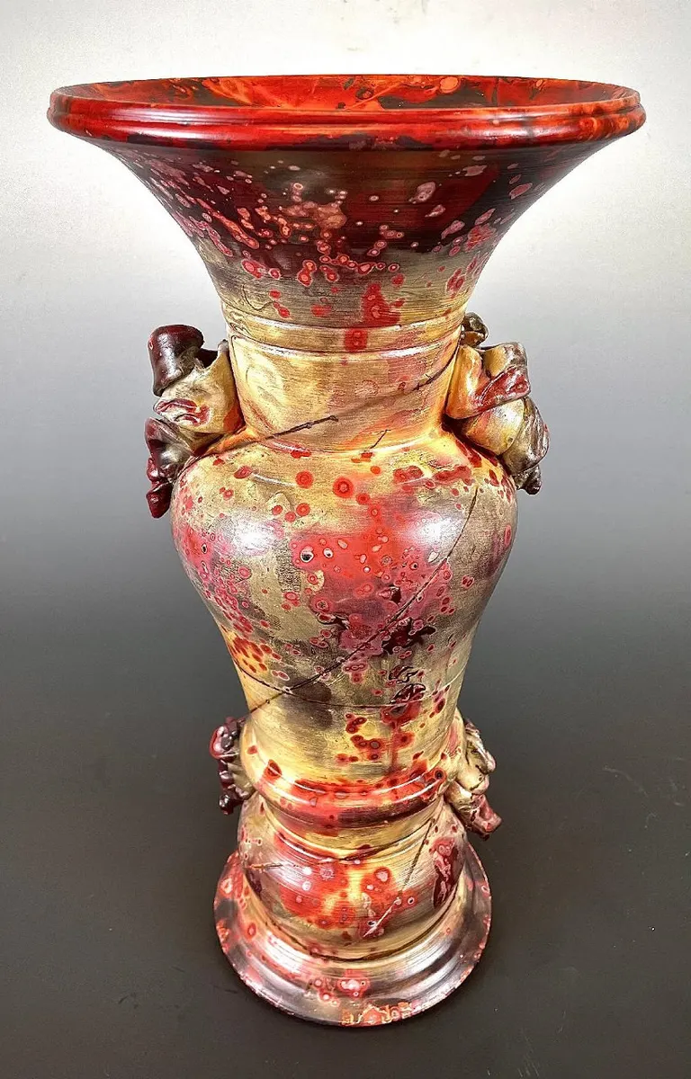 Tall flared vessel in red and cream with sculpted side ornaments