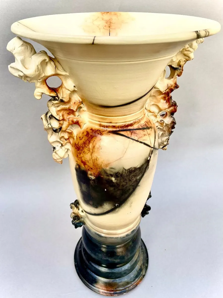 Tall flared vessel in cream and black with sculpted ornament at the rim